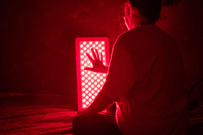 Senior Woman touching Red Light Therapy Panel LEDs with hand red light therapy panel